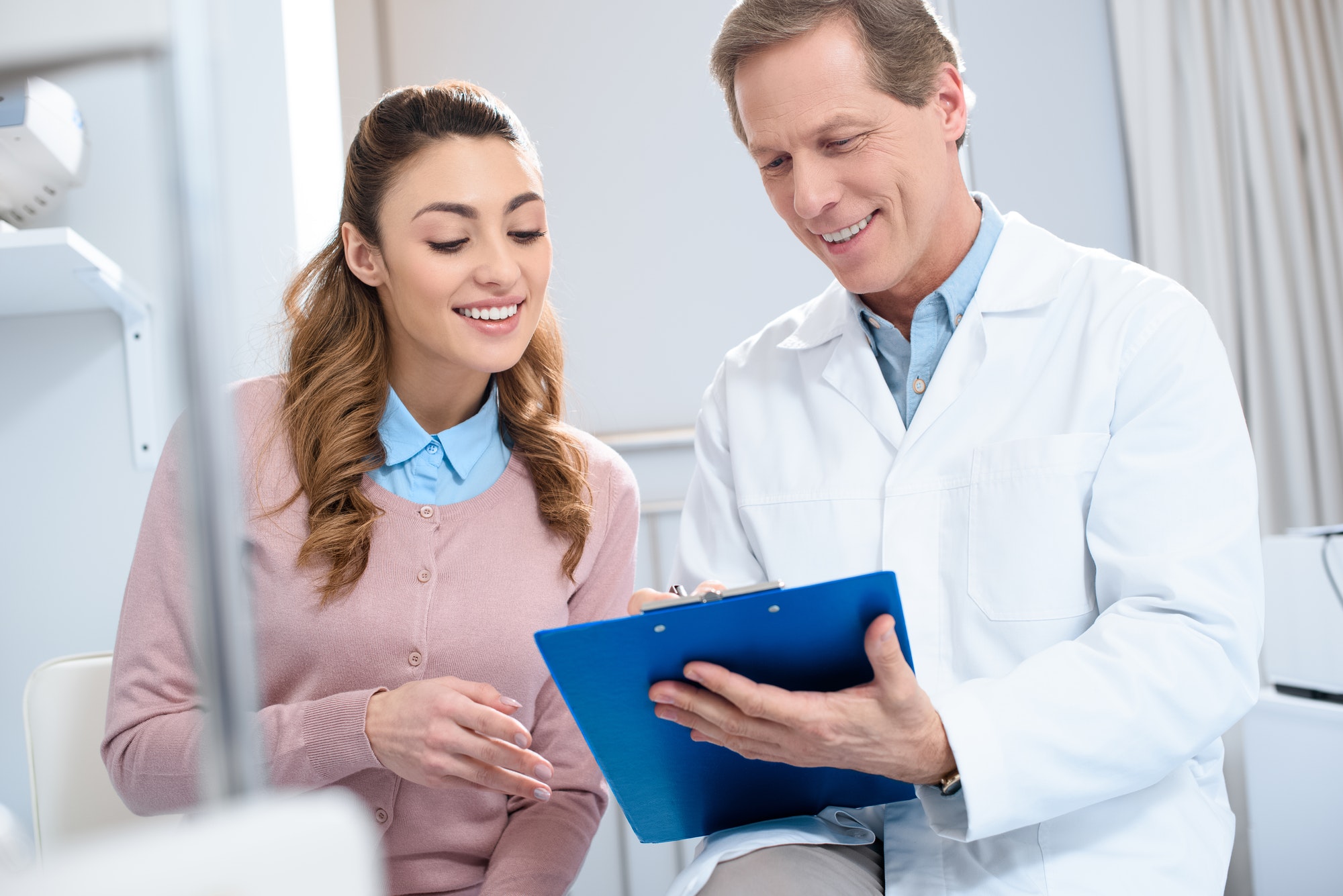 handsome-doctor-showing-something-in-clipboard-to-smiling-patient-in-clinic.jpg